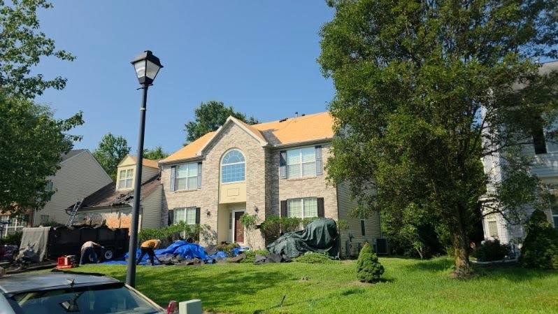 Tarps and a dump trailer staged around a brick colonial during a full roof tear-off in Laurel, MD