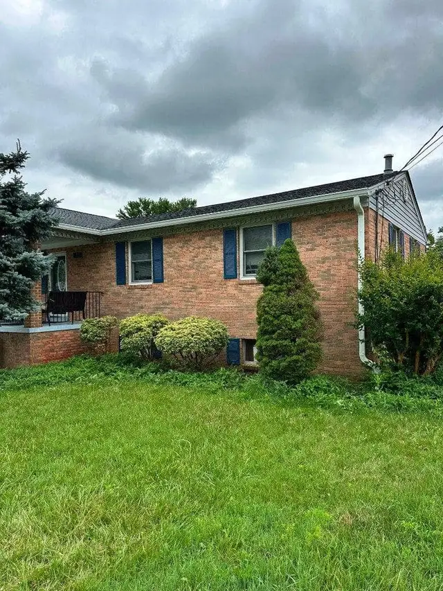 Gutter installation on a brick rambler home with blue shutters