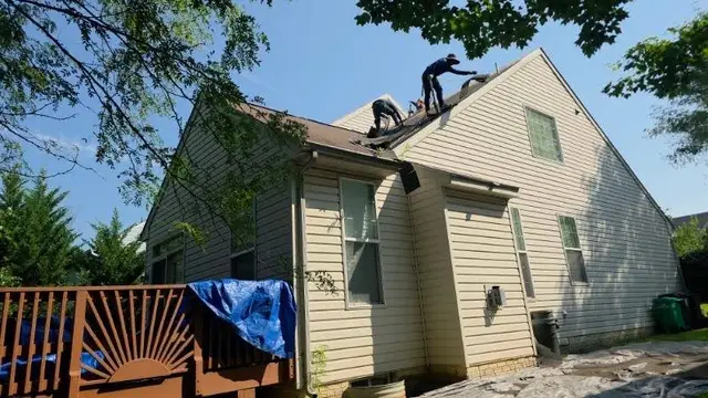 Roofing crew tearing off old shingles on a two-story home with the deck tarped below