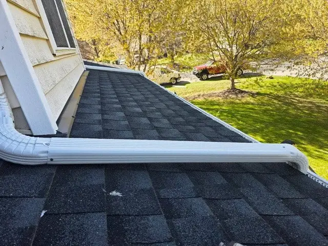 Seamless gutter and downspout installed along a shingle roof edge